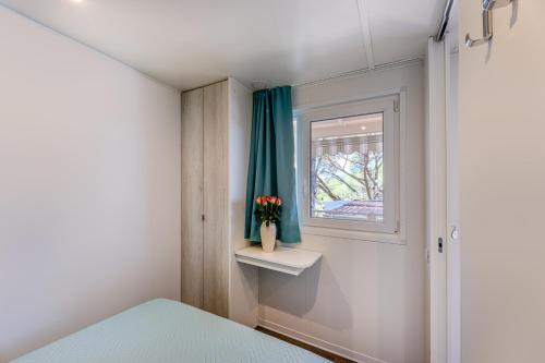 a small bedroom with a window and a vase with flowers at Camping Bungalow Lido in Capoliveri