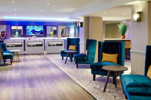 a waiting room with blue chairs and a bar at Hanbury Manor Marriott Hotel & Country Club in Ware