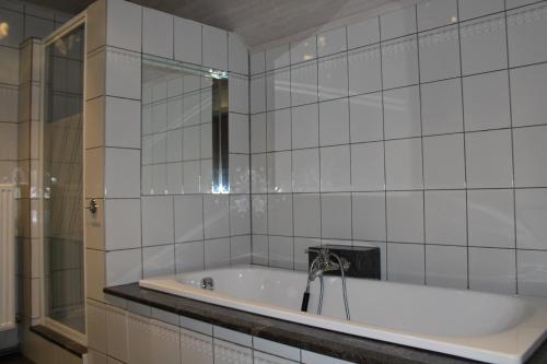 a white tiled bathroom with a tub and a mirror at Villa Luna in Oudsbergen 