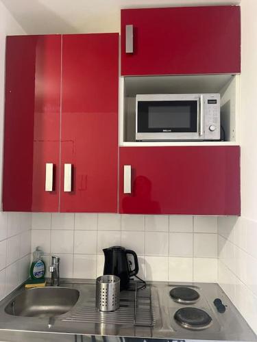La cuisine est équipée de placards rouges, d'un évier et d'un four micro-ondes. dans l'établissement Studio proche Disney et Paris, à Noisy-le-Grand