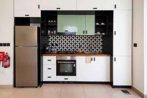 a kitchen with white cabinets and a refrigerator at Socio Tower1 - Dubai Hills Modern Urban Retreat in the City by Serenity Living Holiday Homes in Dubai