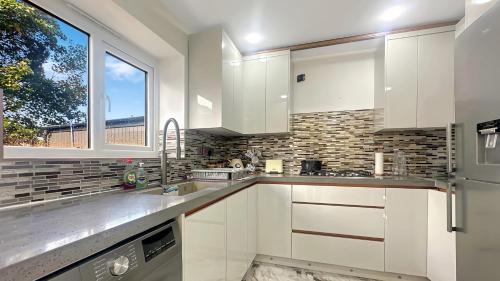 a kitchen with white cabinets and a window at 4 Bedroom Excellent Home Large Spacious Layout Detached House Driveway Free Parking in Stockport