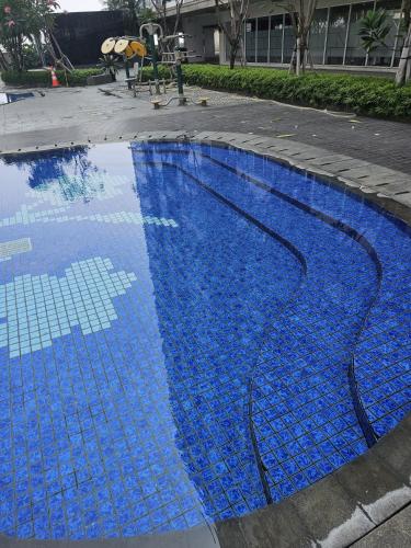 a blue swimming pool with blue tiles on the ground at Green Sedayu Apartment Family Suite by Ellison in Jakarta