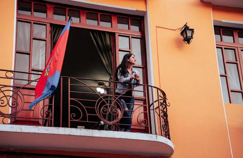 a woman standing on a balcony with a flag at La Posada Colonial in Quito