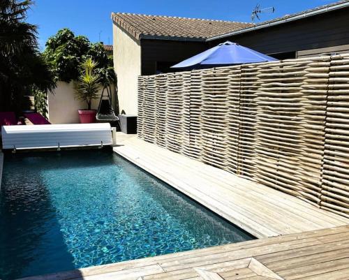 - une piscine avec une clôture en bois et un parasol dans l'établissement Maison des sables piscine chauffée 2 chambres 100m des plages, à Angoulins-sur-Mer