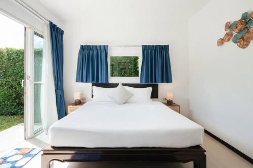 a bedroom with a large white bed with blue curtains at Tranquil 3 Bedroom Garden Pool Villa in Laguna Phuket