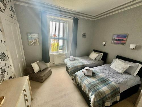 a bedroom with two beds and a chair and a window at Bayside - Breathtaking views of the Clyde in Rothesay