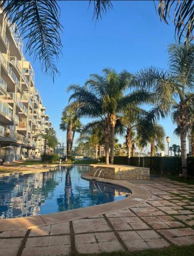 a swimming pool with palm trees and a building at Apartamento en Moncofa in Moncófar