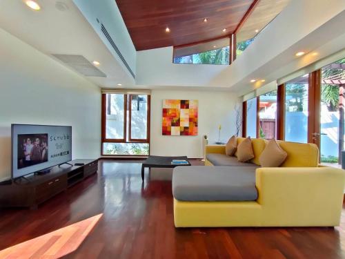 a living room with a yellow couch and a tv at Pranaluxe 4 Bedroom Pool Villa C8 in Pran Buri