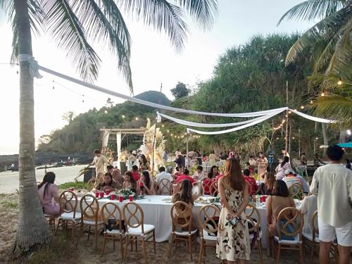 eine Gruppe von Menschen sitzt um einen Tisch am Strand in der Unterkunft Longbeach Bungalow Kohmook in Ko Mook