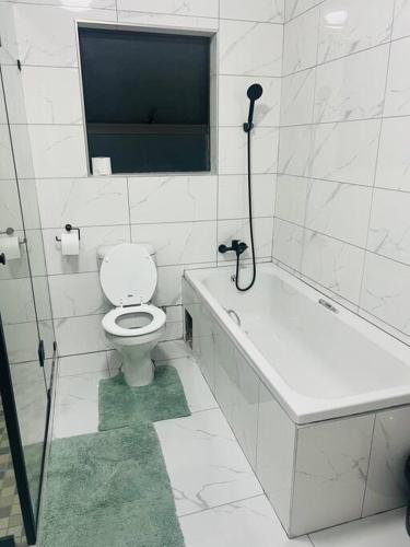 a white bathroom with a toilet and a bath tub at KT Comfort in Midrand