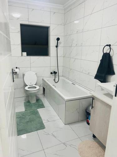 a white bathroom with a toilet and a tub and a tv at KT Comfort in Midrand