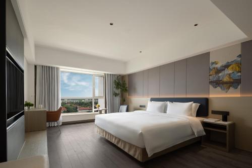 a bedroom with a large bed and a large window at BlueVisual Hotel Zhengzhou Airport in Zhengzhou Xinzheng International AIrport