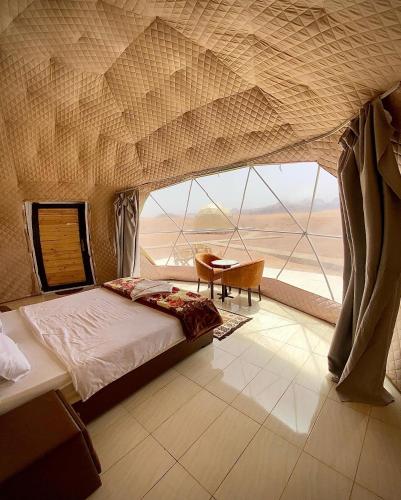 a bedroom with a bed and a table and a large window at Wadi Rum The ARC camp in Wadi Rum