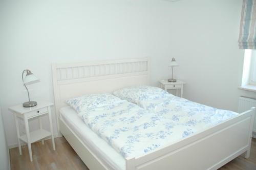 ein weißes Bett in einem weißen Zimmer mit 2 Tischen in der Unterkunft Boardinghouse in Büsum