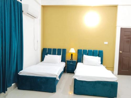 two beds in a room with blue curtains at Victoria Guest House in Bahawalpur