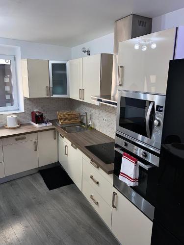 une cuisine avec des armoires blanches, un évier et un micro-ondes dans l'établissement Maison de ville COSY, à Bourg-Saint-Andéol