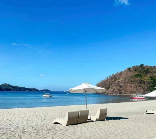 two white chairs and an umbrella on a beach at Jacana B 603 at Pico de Loro by Raquel's Place in Cutad