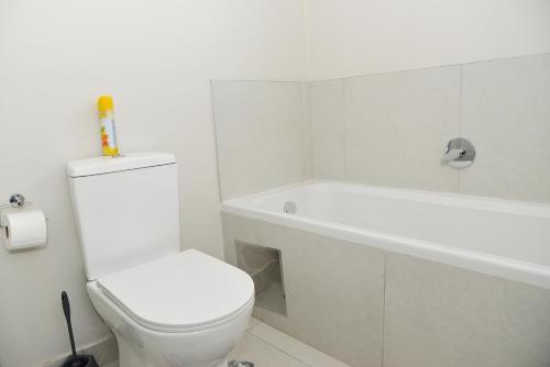 a white bathroom with a toilet and a bath tub at Eirini Elegant - Hermes Apartment in Midrand