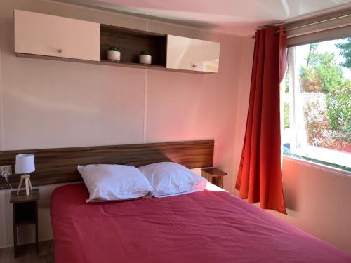 ein Schlafzimmer mit einem Bett mit roten Laken und einem Fenster in der Unterkunft ESCALE BASSIN- Mobile Home Lège Cap-Ferret - Village 4 étoiles LES VIVIERS in Lège-Cap-Ferret