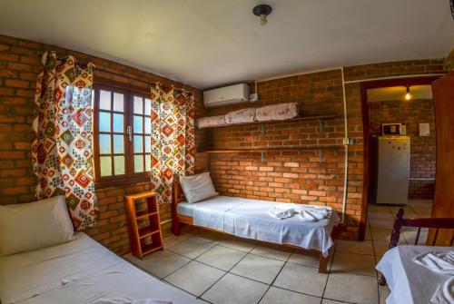 Habitación con pared de ladrillo, cama y nevera. en Pousada Recanto do Rosa, en Praia do Rosa