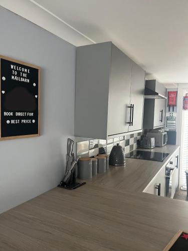 a kitchen with white cabinets and a sign on the wall at The Mail Barn in Lamlash
