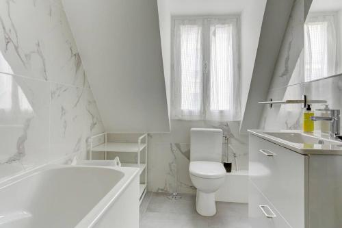 La salle de bains blanche est pourvue d'une baignoire, de toilettes et d'un lavabo. dans l'établissement Le Duplex, à Versailles