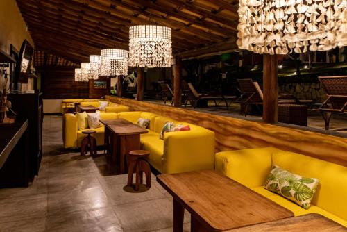 a restaurant with yellow couches and tables and chandeliers at Hotel Villaggio Tudo Bom in Uruau