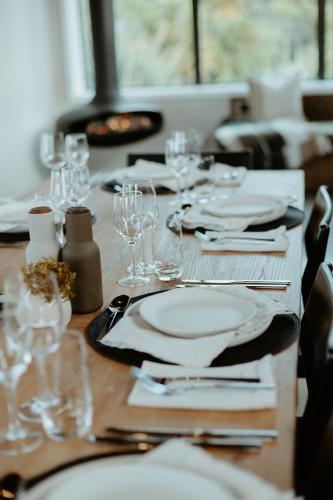 a wooden table with white plates and wine glasses at Te Whaanga Retreat & Spa in Raglan