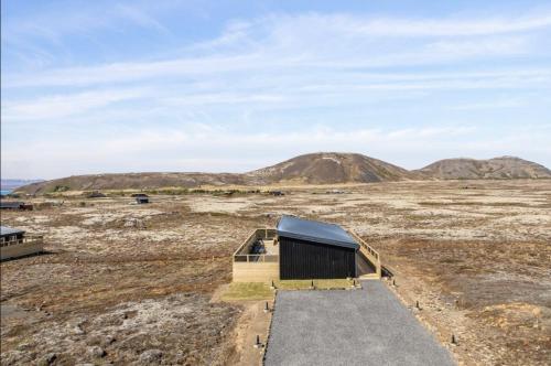 a small building in a field with mountains in the background at Þingvallavatn Hot Tub Sauna 2024 Built Cabin in Veiðilundur