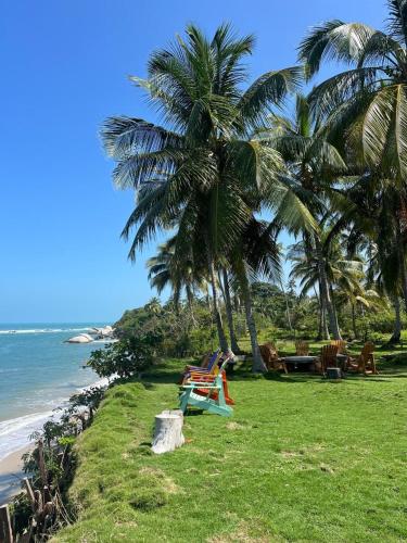 a beach with palm trees and chairs and the ocean at Arrecifes Refugio Natural in Santa Marta