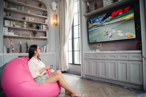 a woman sitting in a pink chair watching tv at The Salil Hotel Sukhumvit 57 - Thonglor in Bangkok