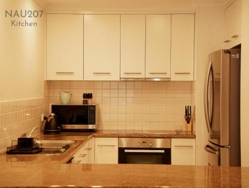 a kitchen with white cabinets and a stainless steel refrigerator at Nautilos On The Harbour in Newcastle