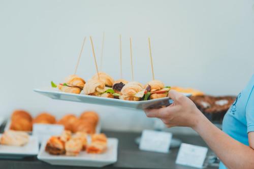 a person holding a tray of pastries and a plate of donuts at AHG Riva Del Sole Hotel - Adults Only in Moniga