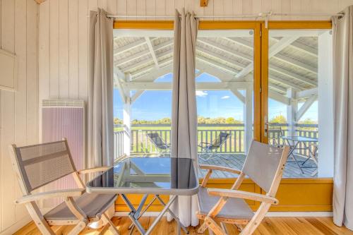 2 chaises et une table en verre devant une fenêtre dans l'établissement 1 maison et son studio sur pilotis, à Talais