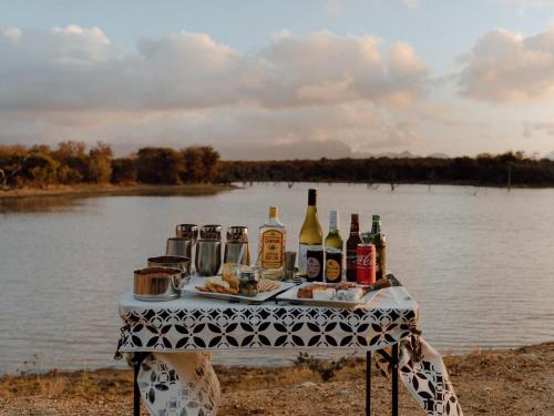 a table with bottles of alcohol and food on it next to a river at Leopard's Bend Bush Lodge in Hoedspruit