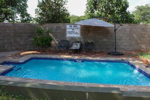 ein Swimmingpool mit zwei Stühlen und einem Sonnenschirm in der Unterkunft Lulu Guest Lodge, Low-Density Suburbs, Victoria Falls in Victoriafälle