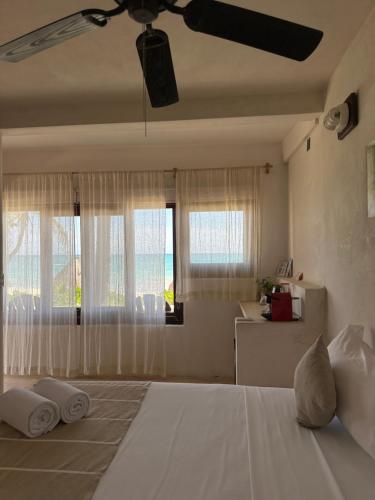 a bedroom with a bed with a ceiling fan and windows at La Conchita Tulum in Tulum
