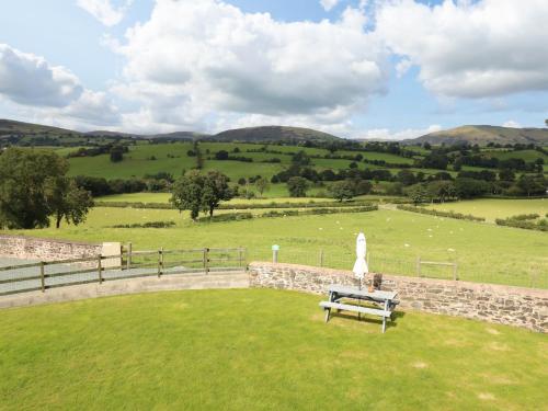 a bench sitting in the grass with a field and hills at Bwthyn Y Bugail Shepherd's Cottage in Oswestry