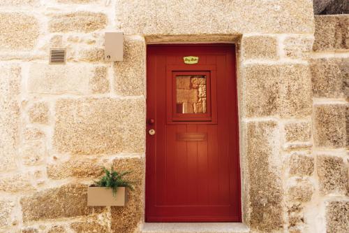 a red door in a stone building with a plant at Story Studio Sortelha - Heritage in Sortelha