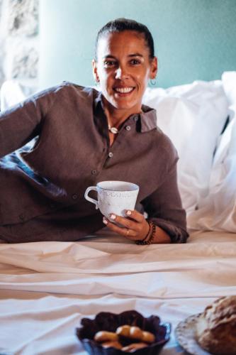 a man sitting on a bed holding a cup of coffee at Story Studio Sortelha - Heritage in Sortelha
