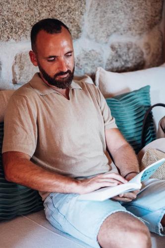 a man sitting on a couch reading a book at Story Studio Sortelha - Heritage in Sortelha
