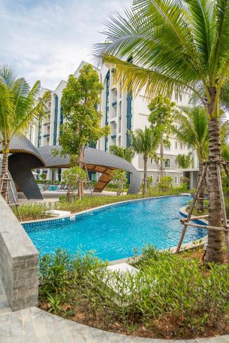 a swimming pool with palm trees in front of a building at Title Halo Nature Touch 40m2 King Bed Naiyang in Nai Yang Beach