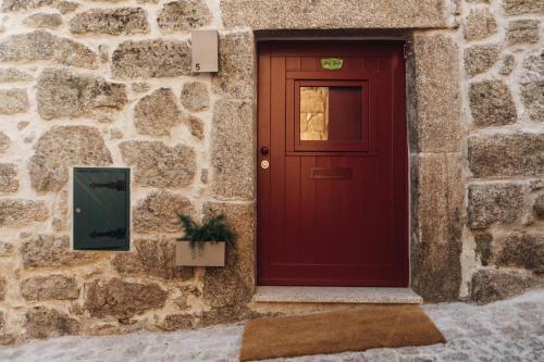 a red door on the side of a stone building at Story Studio Sortelha - Heritage in Sortelha