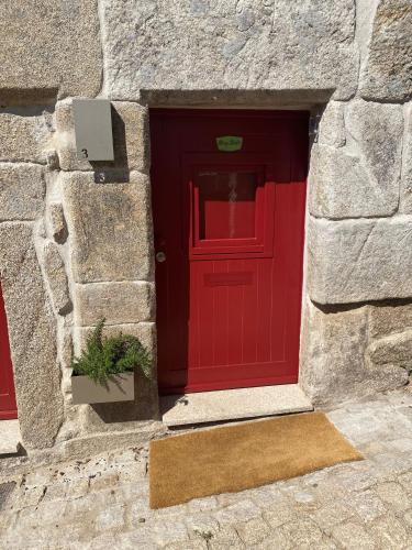 a red door in a stone building with a potted plant at Story Studio Sortelha - Heritage in Sortelha