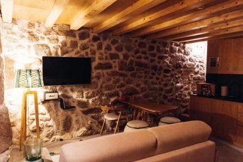 a living room with a couch and a tv on a stone wall at Story Studio Sortelha - Heritage in Sortelha