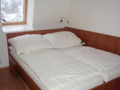 1 cama con cabecero de madera y almohadas blancas en Apartmán Ramzová B14, en Ramzová