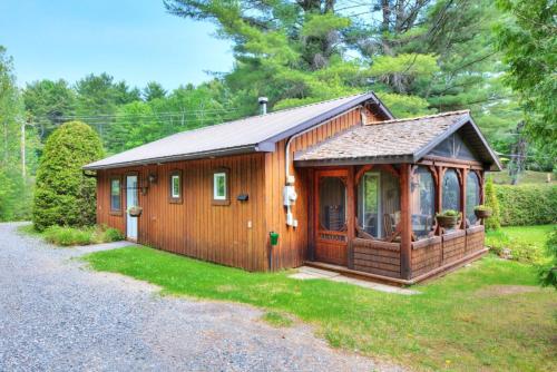 a small wooden cabin with a porch in the grass at Domaine Chalets des pins in Rawdon