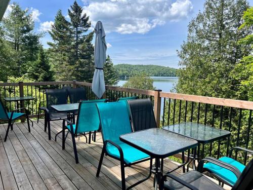 a deck with tables and chairs and an umbrella at Chalet Mon Repos - Lac Sarrazin avec embarcations in Sainte-Lucie-de-Doncaster
