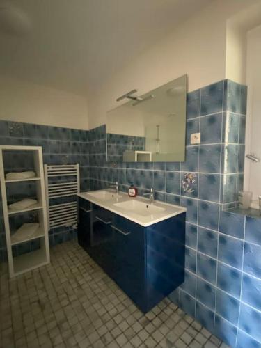 La salle de bains est pourvue de carrelage bleu, d'un lavabo et d'un miroir. dans l'établissement La Maison de Marie, à La Boissière-sur-Evre